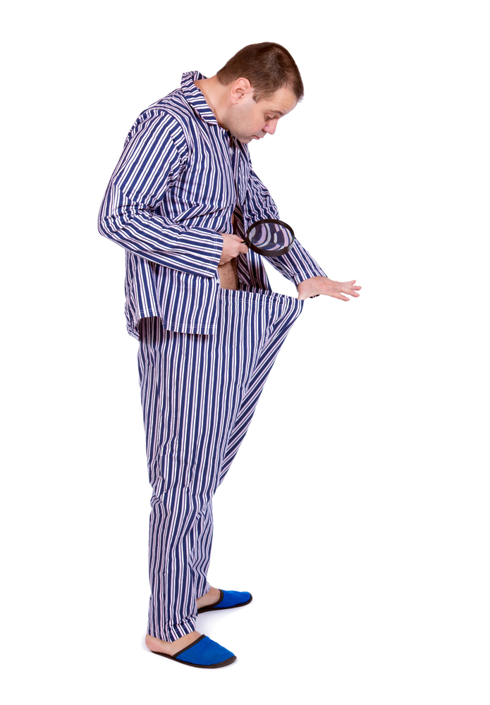 A man in striped pajamas looks into his pants with a magnifying glass.